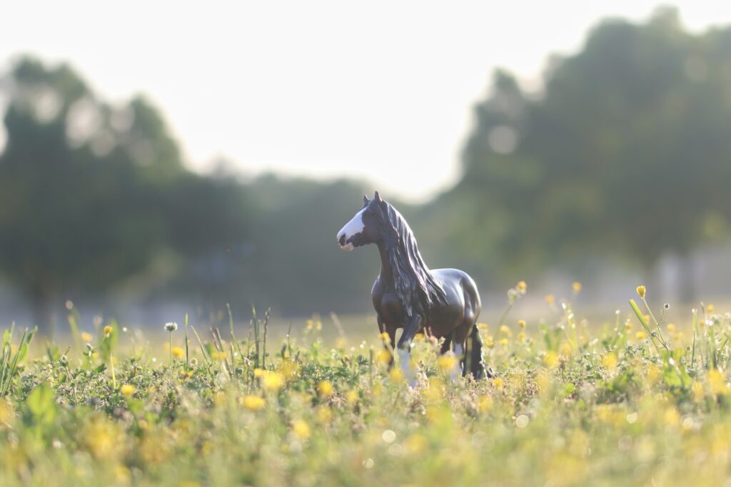 Model horse walking in green and yellow field.